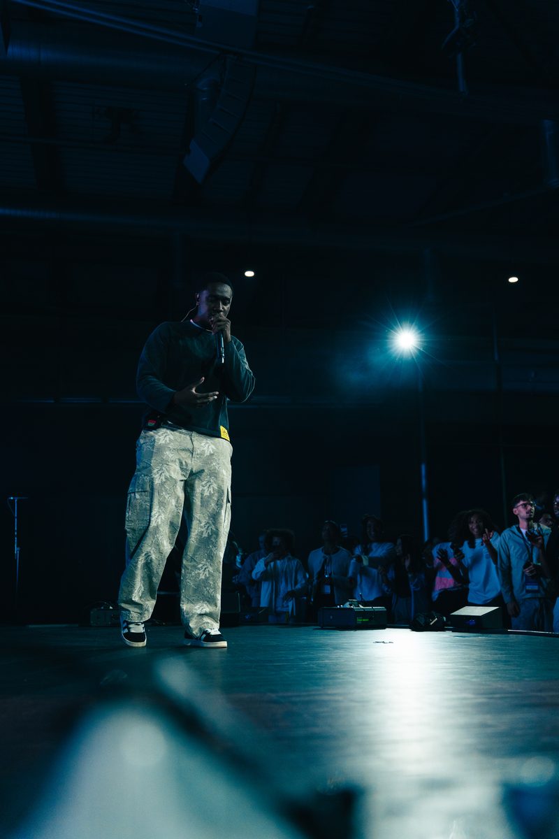 Rapper geht im blauen Licht über die Bühne, Publikum am Bühnenrand