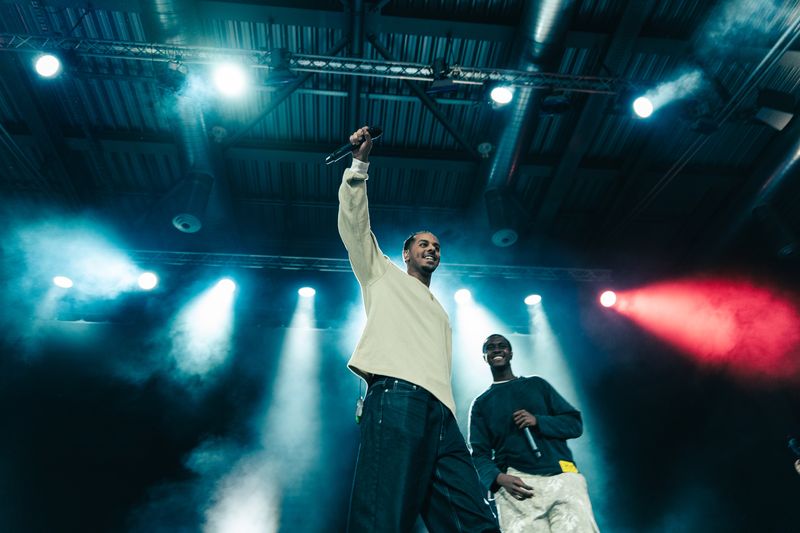 Zwei Rapper auf der Bühne, einer mit erhobenem Arm im Gegenlicht